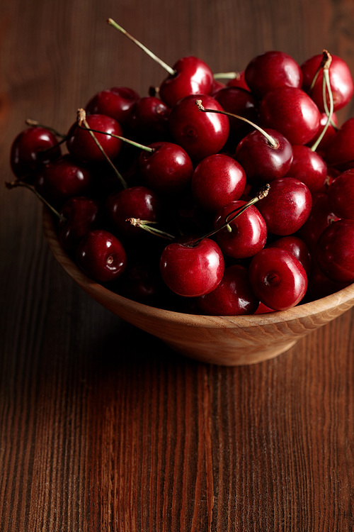 wooden bowl with red ripe cherries on wooden brown table