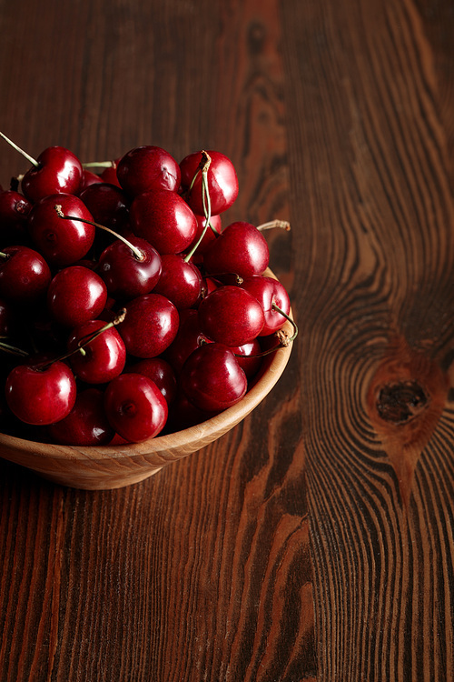 red delicious cherries in wooden bowl on wooden brown table