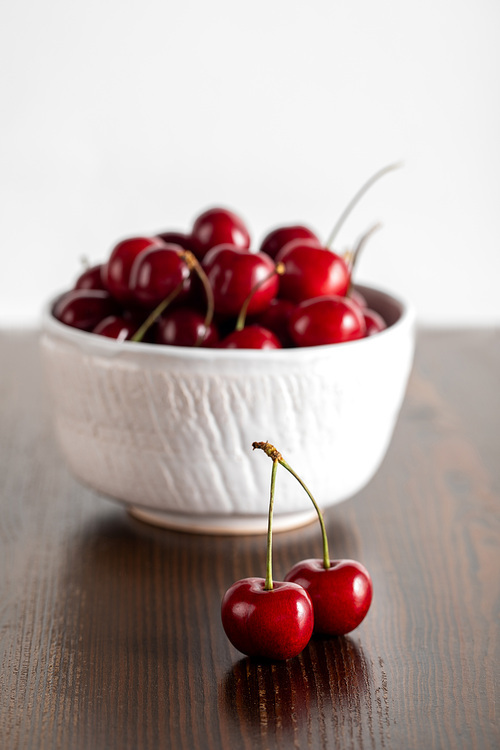 selective focus of red cherries in white bowl on wooden table isolated on white