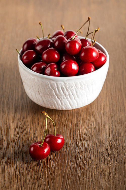 selective focus of red cherries in white bowl on wooden table