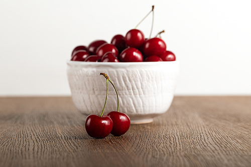 selective focus of red cherries in bowl on wooden table isolated on white