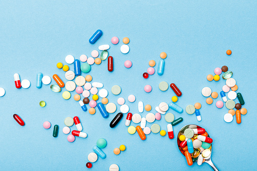 Top view of colorful pills and spoon on blue surface