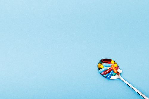 Top view of colorful pills and spoon on blue surface