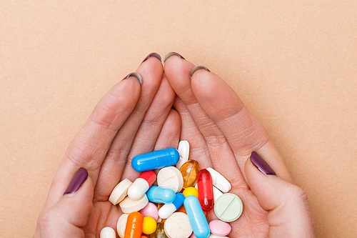 Partial view of woman holding colorful pills in hands on brown