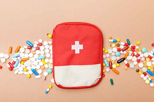 Top view of first aid kit bag and colorful pills on brown surface