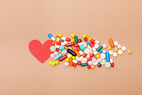 Top view of colorful pills and paper heart on brown surface
