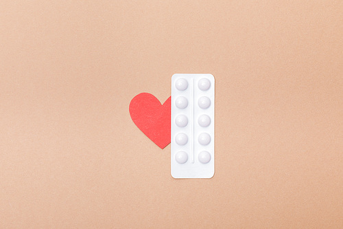Top view of blister with pills and paper heart isolated on brown
