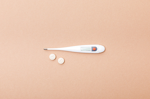 Top view of thermometer and pills on brown surface