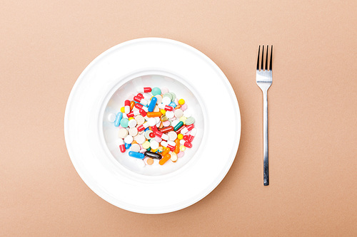Top view of bowl with pills and fork on brown surface