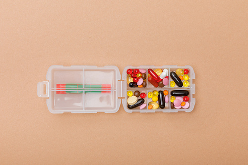 Top view of container with colorful pills on brown surface