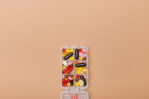 Top view of container with colorful pills on brown surface