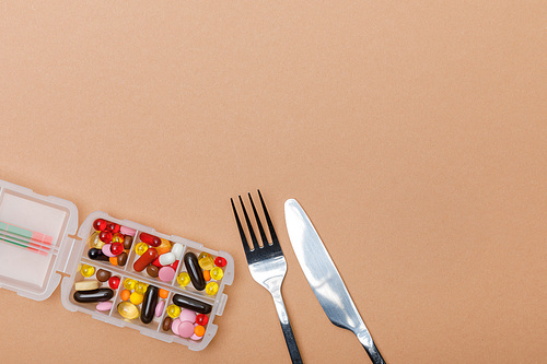 Top view of container with pills and cutlery on brown surface