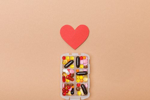 Top view of container with pills and paper heart on brown surface