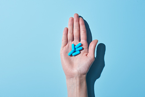 cropped view of woman holding blue pills on palm on blue background