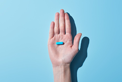 cropped view of woman holding blue pill on palm on blue background