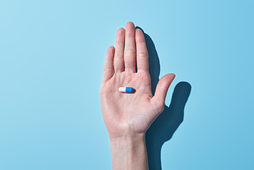 cropped view of woman holding blue and white pill on palm on blue background