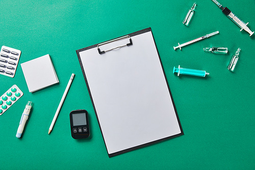 top view of pencil on folder with blank paper rounded by various medical supplies on green surface
