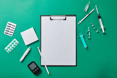 top view of pencil on folder with blank paper rounded by various medical supplies on green background