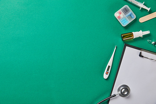syringe, wooden tongue depressor, ampule, pill box, nasal spray, thermometer, stethoscope and folder on green background