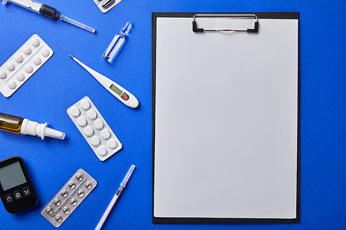 top view of folder with blank paper rounded by various medical supplies isolated on blue