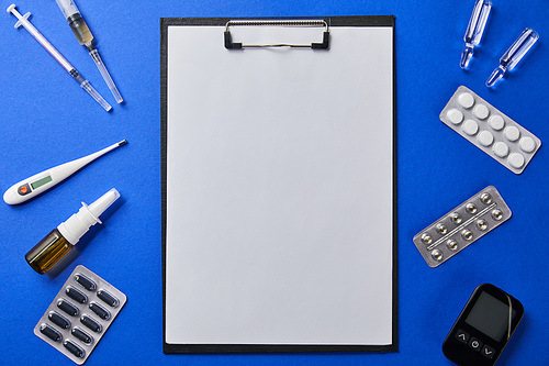 top view of folder with blank paper rounded by various medical supplies on blue surface