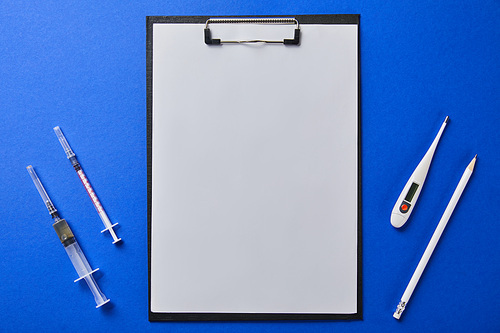 top view of syringes, thermometer and pencil near folder with blank paper isolated on blue