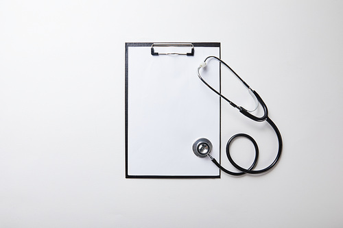 top view of clipboard with stethoscope on white surface