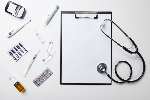 top view of various medical supplies near folder with blank paper and stethoscope on white