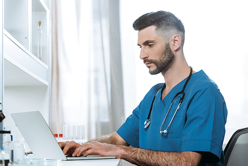 young doctor with stethoscope on neck typing on laptop