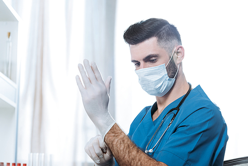 young doctor in medical mask putting on protective latex gloves