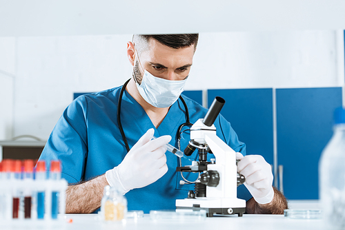 selective focus of biologist in medical mask and latex gloves holding syringe near microscope