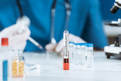 selective focus of test tube with coronavirus inscription near scientist and glass containers with medicines