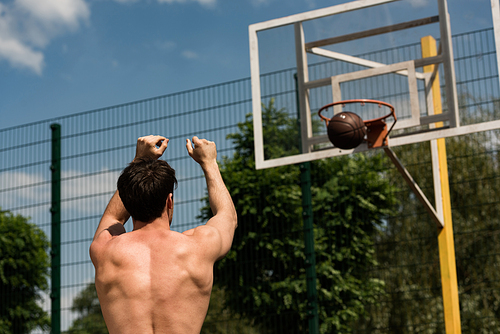 back view of shirtless basketball player throwing ball in basket at basketball court