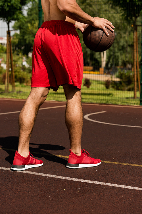 partial view of basketball player with ball at basketball court in sunny day