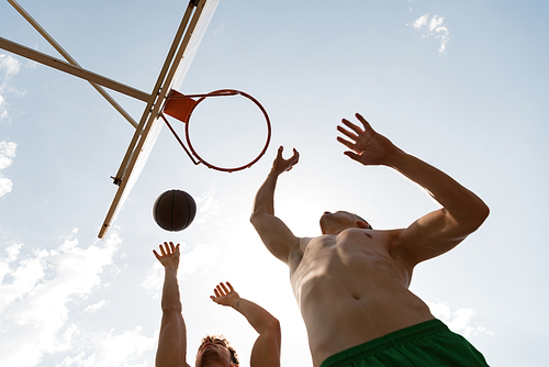 bottom view of shirtless basketball players throwing ball in basket in sunny day