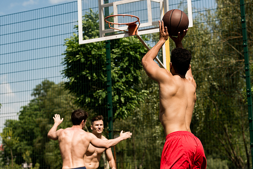 shirtless sportsmen playing basketball at basketball court in sunny day