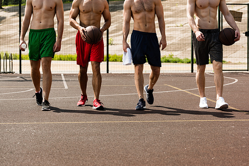 cropped view of four shirtless basketball players with balls at basketball court