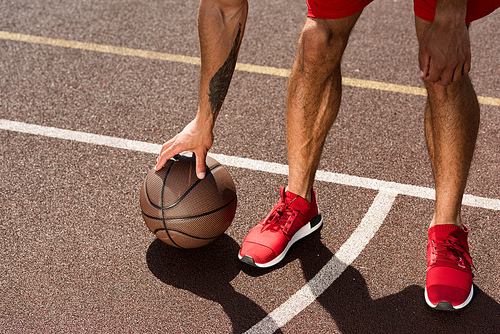 cropped view of sportsman in red sneakers with ball at basketball court