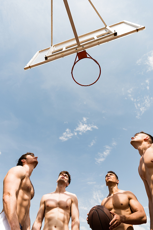 bottom view of shirtless sportsmen playing basketball under blue sky