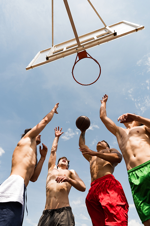 bottom view of shirtless sportsmen playing basketball under blue sky
