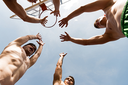 bottom view of four shirtless sportsmen raising hands under sky near basketball backboard