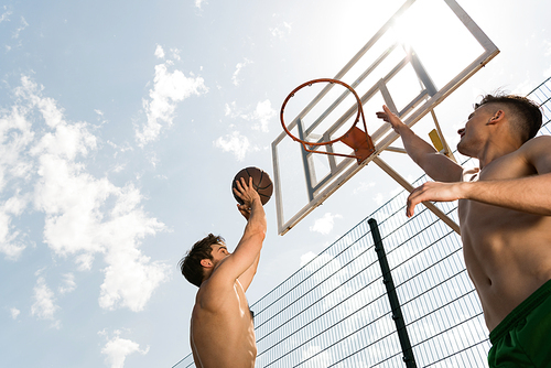 two sexy shirtless sportsmen playing basketball under blue sky at basketball court