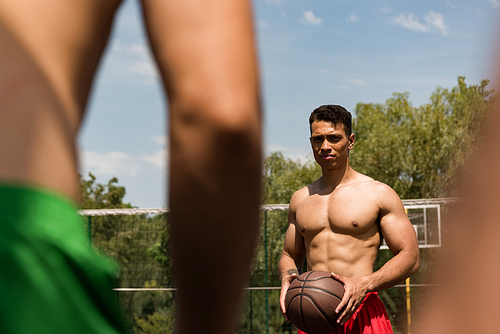 cropped view of sexy shirtless sportsmen playing basketball under blue sky