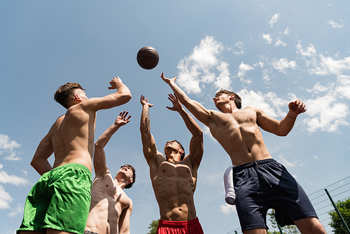 four sexy shirtless sportsmen playing basketball under blue sky