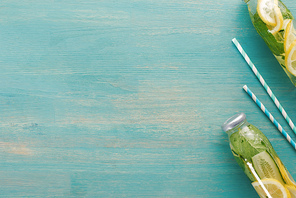 top view of detox drink with lemon, mint and cucumber in bottles near straws