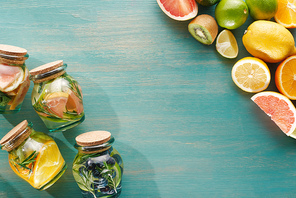 top view of detox drinks in jars with fruits, s, herbs, berries and greenery near fruit ingredients on wooden blue surface