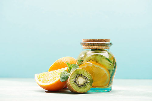 detox drink in jar near kiwi, mint and oranges isolated on blue