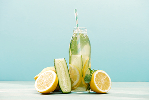 detox drink in bottle with straw near lemons, mint and cucumber isolated on blue