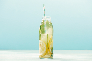 detox drink in bottle with straw, lemons, mint and cucumbers isolated on blue