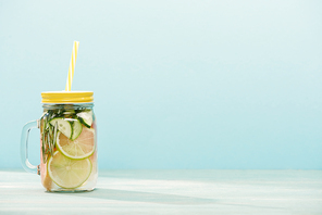 detox drink in jar with lime, cucumber and straw isolated on blue